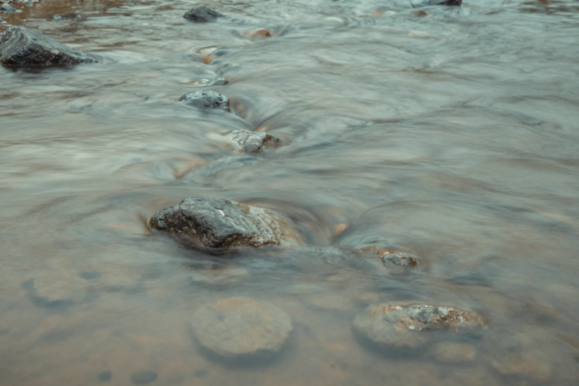 Close-up of clear river water flowing in soft ribbons over smooth stones.