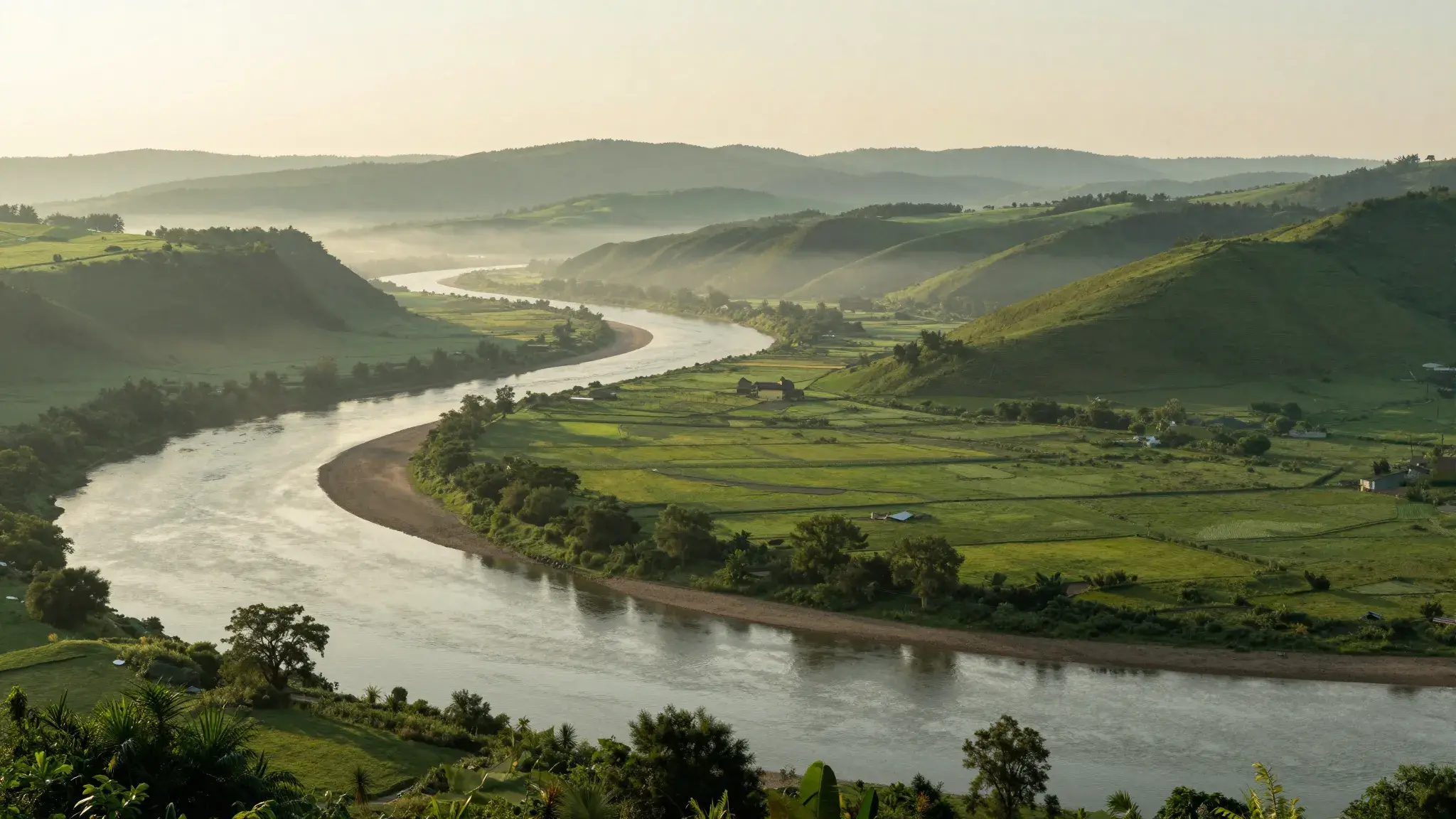 A river winding through a green valley at golden morning light, mist over distant hills.